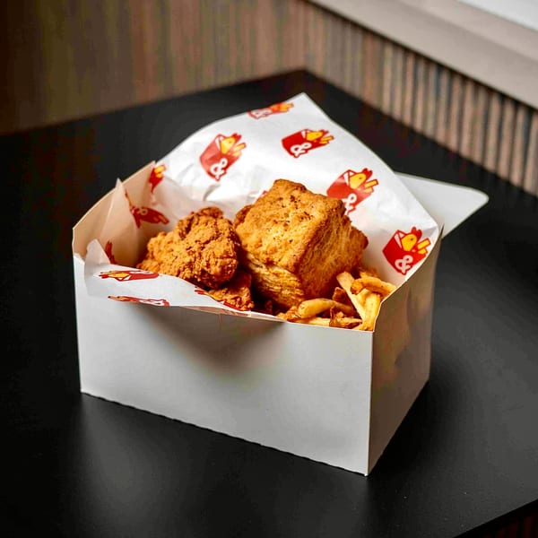 Box & Bird fried chicken tenders, biscuit, and fries in a white box with branded paper.